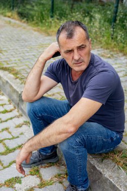 Bir adam kaldırımda oturuyor ve uzaklığa bakıyor.