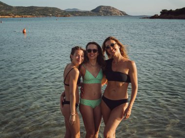 Sardunya sahilinde bikinili üç kadın. Corallina.