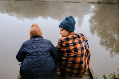 Çocuklar rıhtımda yan yana oturup sakin bir göle bakıyorlar..