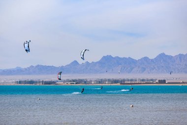 Denizde uçurtmacılar ve arka planda dağlar.