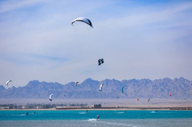 Denizde uçurtmacılar ve arka planda dağlar.