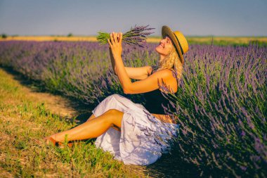Şapkalı bir kadın lavanta tarlasında oturuyor.