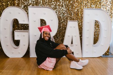 Mezuniyet için pembe şapkalı büyük GRAD tabelalı siyah kız.