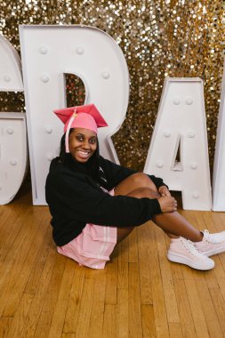 Mezuniyet töreninde şapkalı genç siyah kız mutlu ve gülümsüyor.