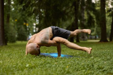 Adam yeşil parkta yoga pozu veriyor.