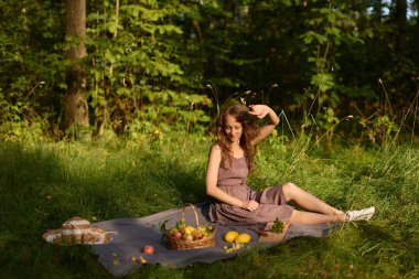 Genç bir kadın güneşli bir günde yemyeşil ormanda piknik yapmaktan hoşlanır.