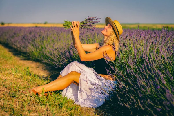 Şapkalı bir kadın lavanta tarlasında oturuyor.