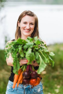 Gülümseyen kadın bir demet taze pancar ve havuç sunuyor.