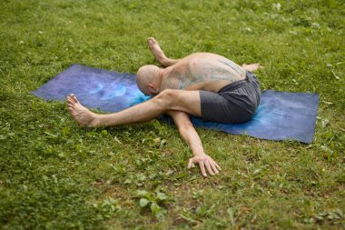 Esnek adam çimenli parkta yoga pozu veriyor.