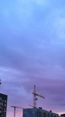 Gün batımında mor ve mavi gökyüzüne karşı inşa edilmiş vinçler.