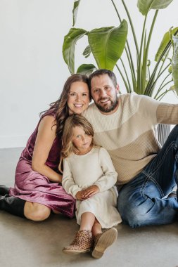 Üç kişilik aile stüdyoda yeşil bitkinin önünde oturur.