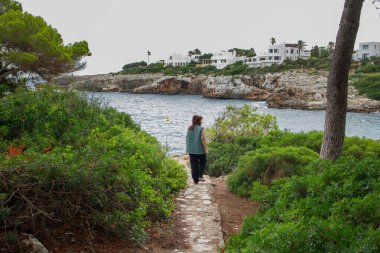 Cala D 'or sahilinde yürürken Mallorca manzarasının tadını çıkaran bir kadın.