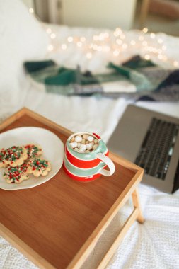 Yatakta Noel kurabiyeleri, sıcak çikolata ve dizüstü bilgisayar.