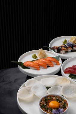 Siyah arka planda beyaz tabakta ton balığı ve somon balıklı Nigiri.