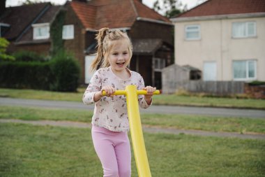 Küçük kız oyun alanında eğleniyor, açık havada çocuk aktiviteleri yapıyor.