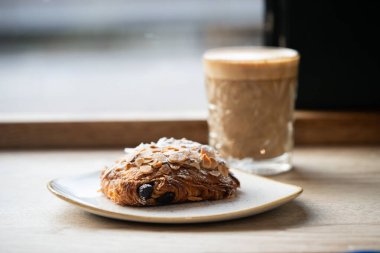Çikolatalı bademli kruvasan ve kafeterya masasında bir bardak kahve.