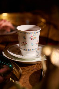 Dekoratif çay fincanı ve çay tabağı düşük ışıkta, ahşap masada.