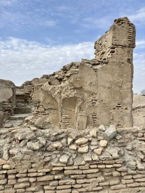 Weathered mud brick & stone ruins of ancient wall against cloudy sky