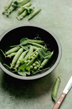 Kabuklu taze bezelyeler ve siyah kasede fasulyeler.