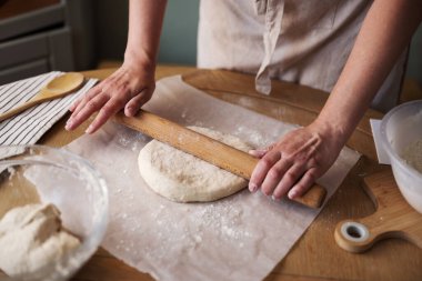 Kadın mutfak masasında hamuru yuvarlıyor, ev yapımı