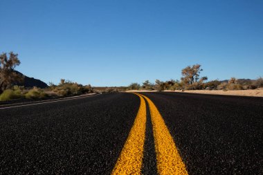Kavisli çöl yolu, berrak gökyüzünün altındaki kurak araziye çıkar.