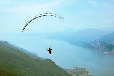 Bir adam dağ gölünün üzerinde bir paraglider üzerinde uçar.