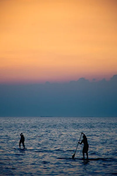サーファーは雲に覆われた夕日を背景にボードを漕いで — ストック写真