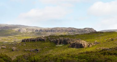 Engebeli Etiyopya Dağları 'nın geniş bir manzarası, çarpıcı antik volkanik kaya kayalıkları ve parlak, bulutlu bir gökyüzünün altında yemyeşil çalılıklarla kaplı oluşumları gösteriyor..