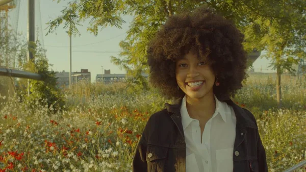 公園の花でいっぱいの混合人種の黒人女性の肖像画。輪郭の太陽の下で笑う — ストック写真