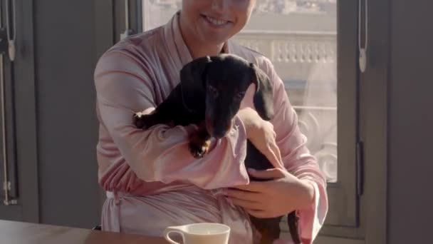 Chica caucásica con una túnica rosa, con un cachorro en las manos en la mañana soleada. Video panorámico de alta calidad 4k metraje. — Vídeo de stock