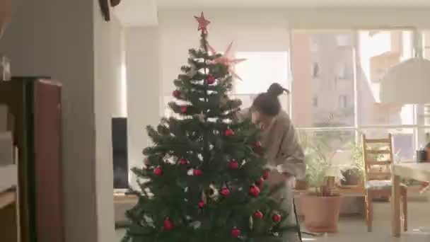 Cabelo escuro mistura raça menina decoração e árvore de Natal artificial em casa. Medium Wide Camera tiro 4k imagens de vídeo de alta qualidade. — Vídeo de Stock