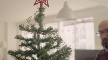 Gözlüklü cesur adam süsleme ve yapay Noel ağacı. Orta ölçekli 4K yüksek kalite video kaydı.