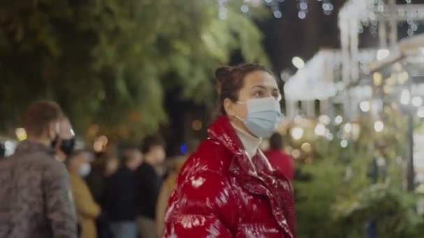 Joven morena en una mascarilla médica mirando alrededor en el mercado de Navidad. Mediano primer plano filmado 4k video de alta calidad. — Vídeos de Stock