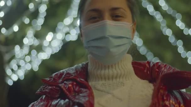 Cerrahi maske takmış genç beyaz bir kadın Noel ışıklarını seyrediyor. 4k video yüksek kaliteli görüntü. — Stok video