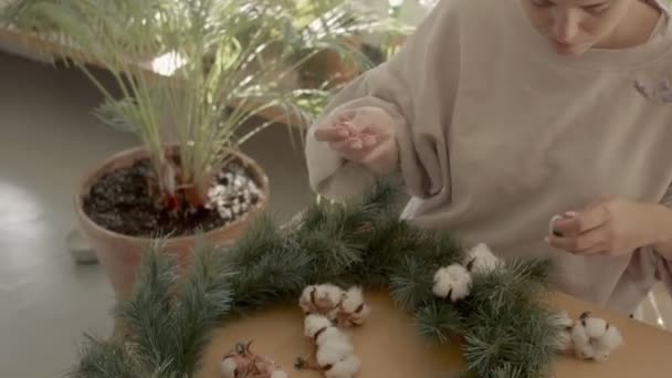 Kaukasische schöne Mädchen macht Weihnachtskranz aus Tannenbaum und Blumen zu Hause. Handled shot 4k qualitativ hochwertiges Videomaterial. — Stockvideo