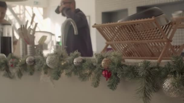 Una pareja tomando café y limpiando el mostrador de la cocina. Decoraciones navideñas. Colores cálidos. 4k metraje de vídeo panorámico. — Vídeos de Stock