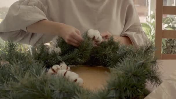 Mujer joven caucásica está haciendo una corona festiva de brunches y flores en casa. Mediano pedestal filmado 4k alta calidad de vídeo. — Vídeos de Stock