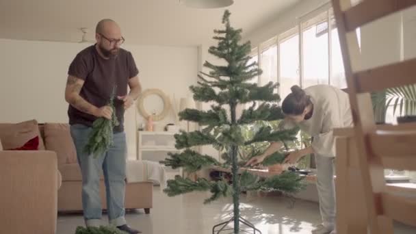 Pareja en un hogar acabado de ropa que componen un árbol de Navidad artificial. Grabación de vídeo 4k de alta calidad de plano completo. — Vídeo de stock