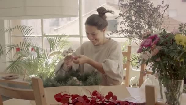 Señora joven caucásica está haciendo una corona festiva con ramas de árbol de piel y algodón en casa. Manejado filmación de vídeo 4k de alta calidad. — Vídeos de Stock