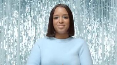 Melez ırkın neşeli portresi, gülen ve altın parıltıları saçan zenci kadın. Orta sahada hala 4K yüksek kaliteli video kaydı var..