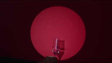 Kırmızı yakut arka planı. Bir el ışıkta bardağı tutar, garson el köpüklü bir içki servisi yapar. Konfeti patlaması. Yüksek kaliteli video görüntüleri.