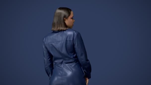 Donna sexy nera con i capelli castano scuro in un abito di pelle blu isolato su sfondo blu profondo. Video 4k di alta qualità. — Video Stock