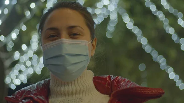 Cabelo escuro jovem mulher em gola alta branca e rosto máscara médica com vista para a cidade de inverno no fundo. Perfil de retrato médio lado tiro. Imagens De Bancos De Imagens Sem Royalties