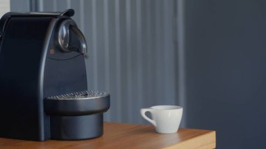 Siyah kompakt otomatik Nespresso kahve makinesi tahta bir masanın üzerindeki küçük beyaz bir seramik bardağın yanında. Yüksek çözünürlüklü jpg resmi.