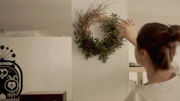 Kafkasyalı genç esmer kadın duvara Noel çelengi asıyor. Görünüm yüksek kaliteli fotoğraf jpg. — Stok fotoğraf