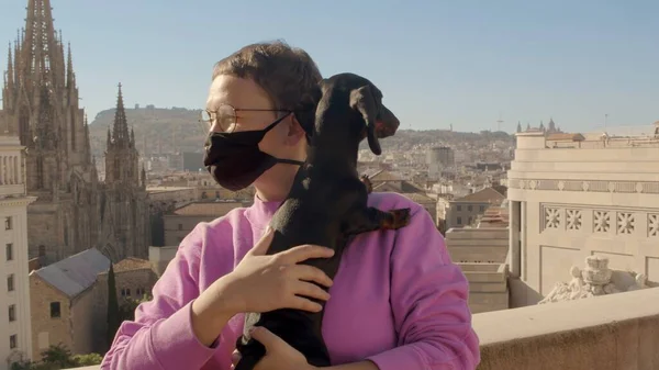 Ragazza con taglio di capelli corto in una maschera covid-19 viso con un cane bassotto sulle mani sta guardando lontano. Alta qualità medio colpo immagine jpg Foto Stock