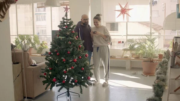 Coppia in una casa indossare guardare arredamento su un albero di Natale artificiale. Immagine fotografica ad alta risoluzione a pieno scatto. Foto Stock