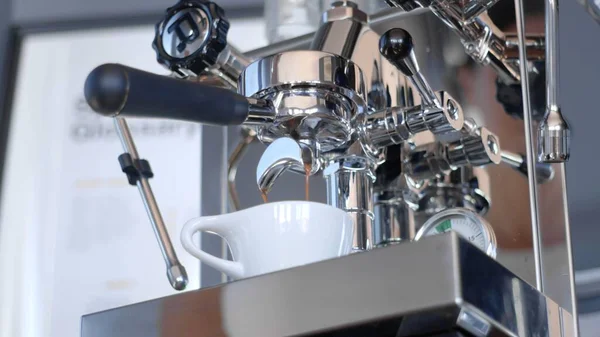 Egy csoport acél kávéfőzőből egy fehér kerámia csészébe extraháljuk az eszpresszót. Alacsony szögű lövés kiváló minőségű fotó. Stock Fotó