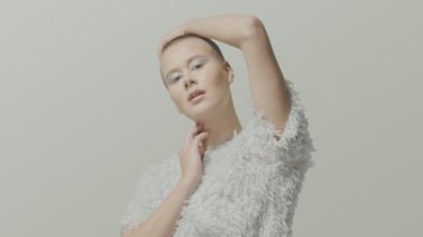 Beyaz elbise stüdyosundaki cesur beyaz kadın model, açık video portresi için poz veriyor.