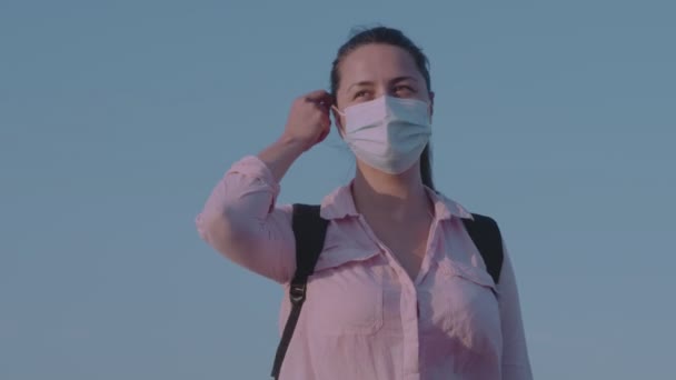 Sabahın erken saatlerinde Kafkasyalı genç bir kadın rüzgârda durur, koruyucu maskesini çıkarır ve keyifle nefes alır. — Stok video